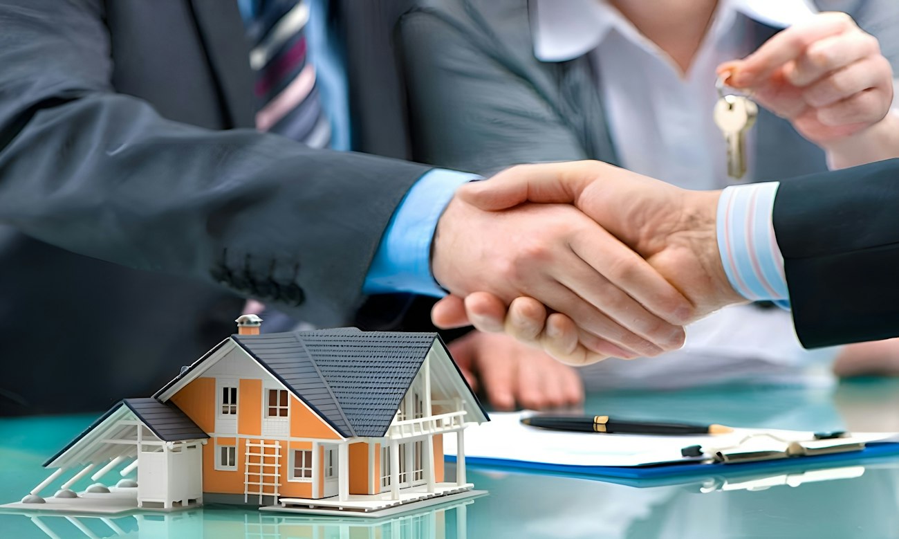 Two people shaking hands over a house model and keys