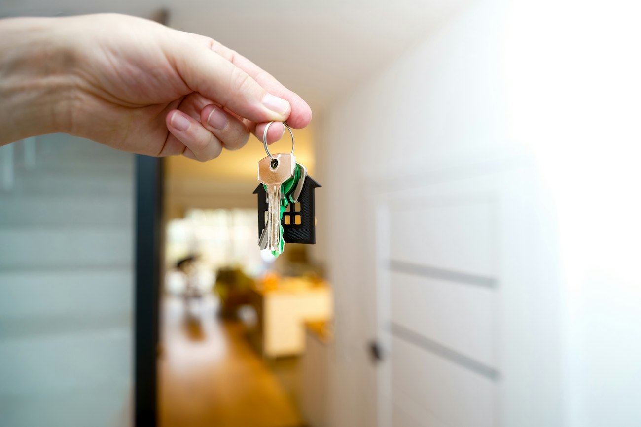 A hand holding house keys in front of an entrance